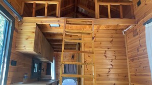 Ein Blockhaus-Innenraum mit Holzwänden, einer Schlafkoje und einer Küche mit Spüle und Arbeitsfläche.