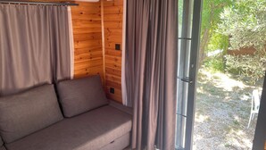 Ein Holzinnenraum mit einer Couch, Vorhängen und einer Schiebeglastür zu einem Außenbereich.