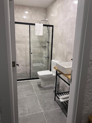 A modern bathroom with a glass-enclosed shower, a white toilet, and a wooden vanity with a sink. - Secret Garden Hotel (Cesme)