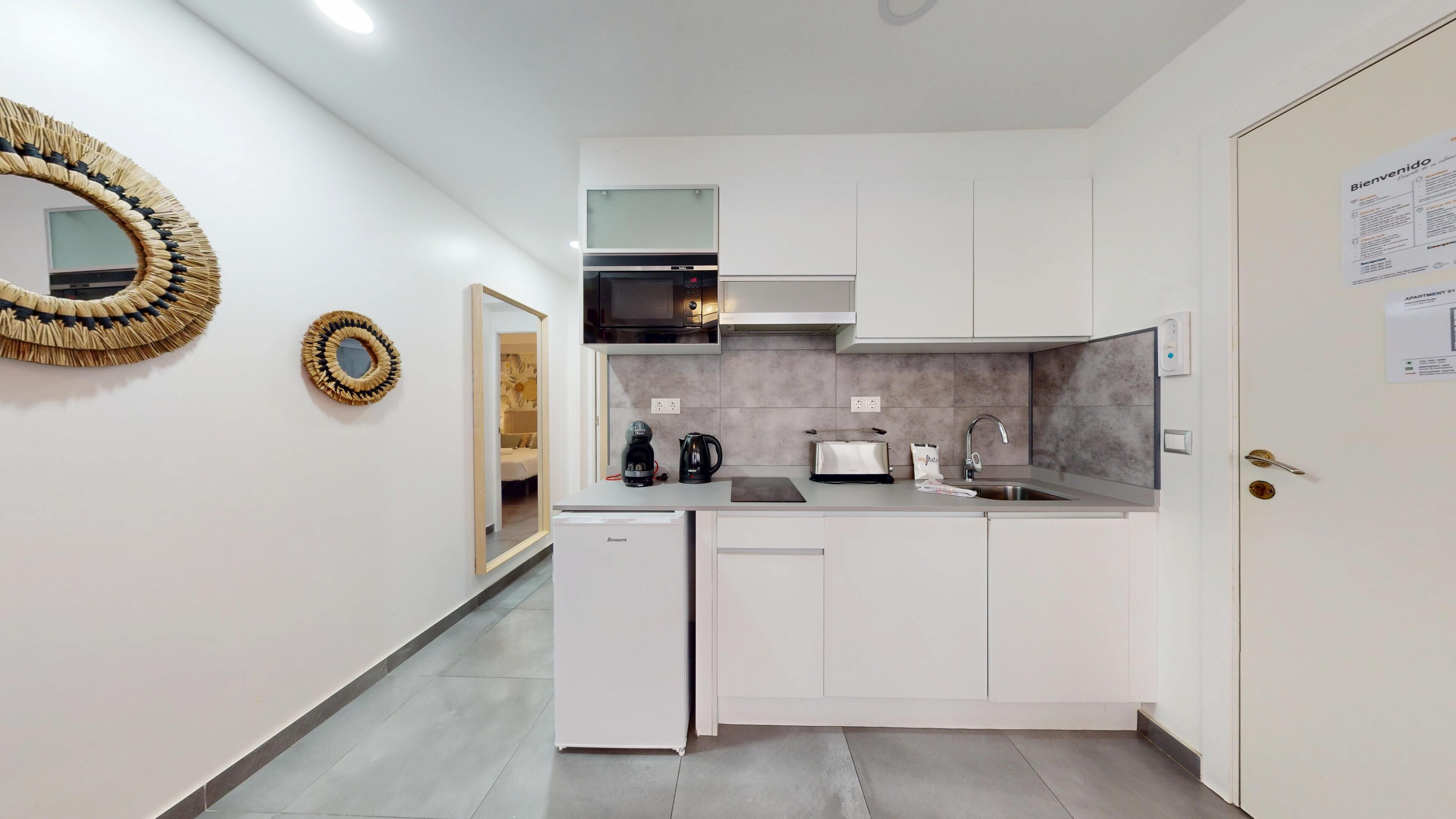 Una cocina moderna con armarios blancos, horno empotrado, cafetera y tostadora.
