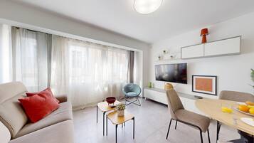 A modern living room with a sofa, a dining table, and a TV mounted on the wall.