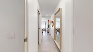 A hallway with a large mirror, a door on the left, and a dining area in the distance. - MyFlats Premium Teatro (Alicante)