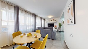 A modern living room with a grey sofa, a TV, and a dining area with a round table and yellow chairs. - MyFlats Premium Teatro (Alicante)