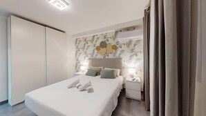 A neatly made bed with towels, a bedside table with a lamp, and a nightstand with a remote control. - MyFlats Premium Teatro (Alicante)