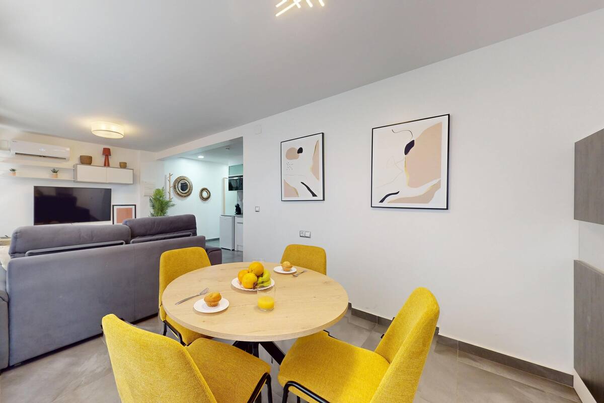 A modern living room with a grey sofa, a dining table with yellow chairs, and artwork on the walls.