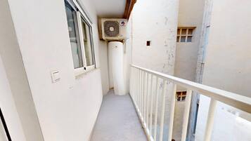 Un balcón estrecho con barandilla blanca, una ventana y un equipo de aire acondicionado instalado en la pared.