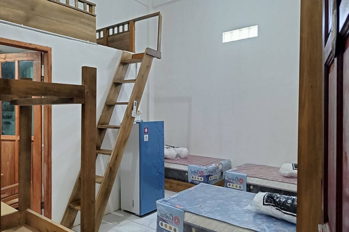 A room with a wooden ladder, a blue refrigerator, and mattresses on the floor.