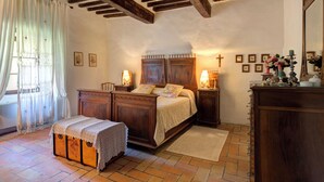 Ein Schlafzimmer mit einem hölzernen Bett, Nachttischen mit Lampen, einer Holzbank und einem Kreuz an der Wand.