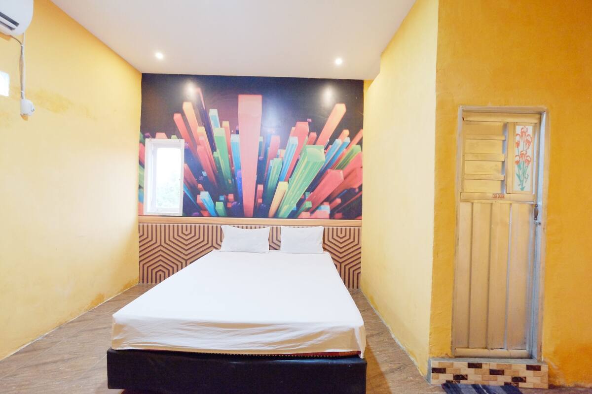 A hotel room with a bed, a colorful abstract mural on the wall, a wooden door, and a patterned floor.