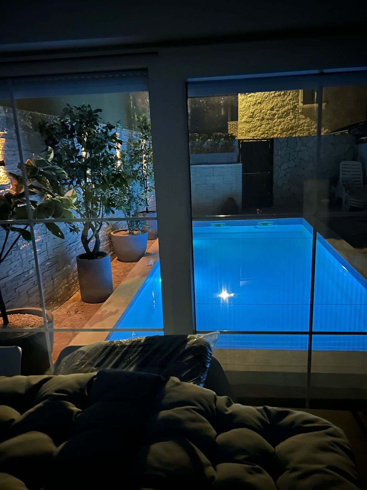 A bedroom with a view of a swimming pool, potted plants, and a brick wall.