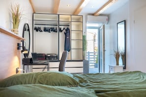 A bedroom with a bed, a desk with a laptop, a chair, a wardrobe, and a window with a view.