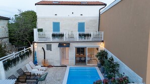 A two-story building with a swimming pool, outdoor seating, and a balcony with blue shutters.