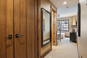 A hallway with wooden doors, a bed, a window, and a desk with a lamp.