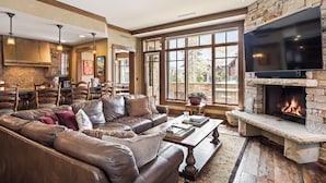 A spacious living room with a leather sofa, a stone fireplace, and a large TV. - Deer Valley Luxury Residence: True Ski-in/ Ski-out, Cozy Interiors, Private Patio (Park City)