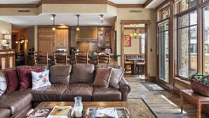 A spacious living room with a leather sofa, wooden dining table, and large windows. - Deer Valley Luxury Residence: True Ski-in/ Ski-out, Cozy Interiors, Private Patio (Park City)