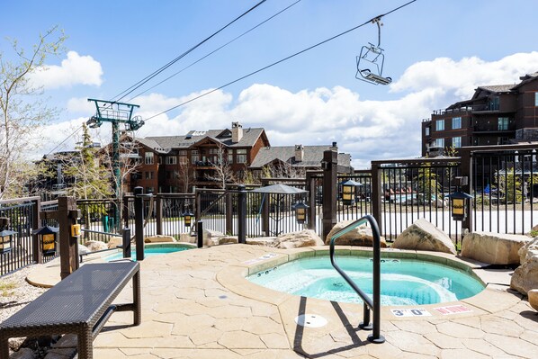 A pool area with a hot tub, a lounge chair, and a ski lift in the background.