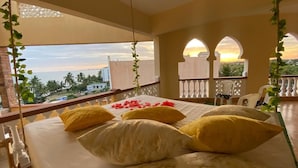 Un balcón con una cama, almohadas amarillas y vista al atardecer.