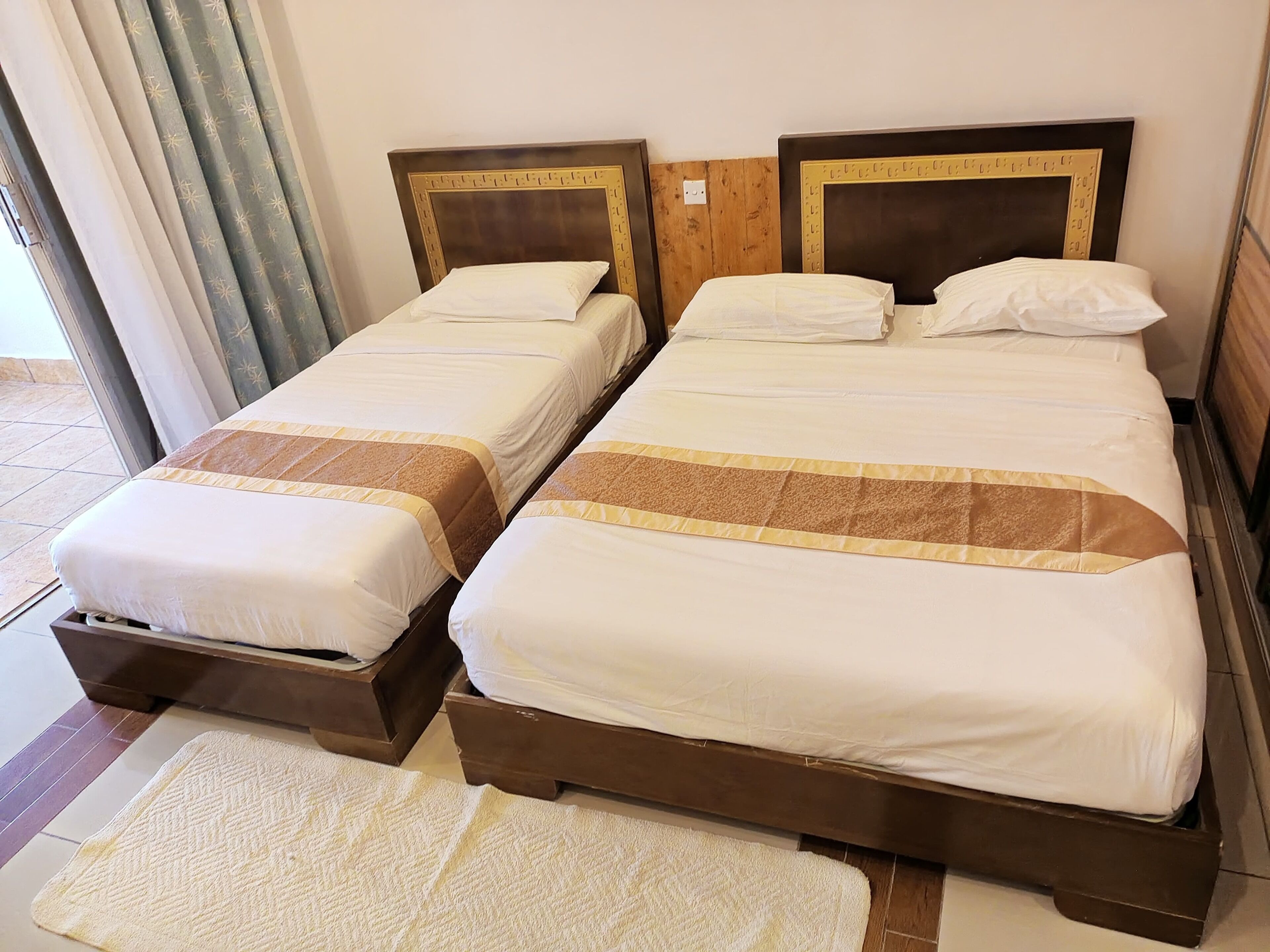 Dos camas individuales con cabeceros de madera y ropa de cama blanca, piso de madera y una ventana con cortinas.