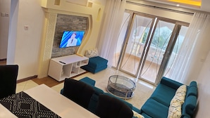Una sala de estar moderna con televisor, sofá y puerta de cristal que da a un balcón.
