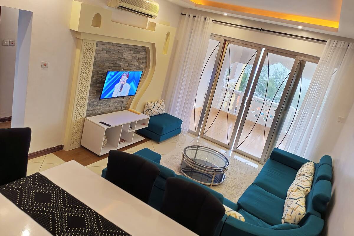 Een moderne woonkamer met een televisie, bank en een glazen deur naar een balkon.