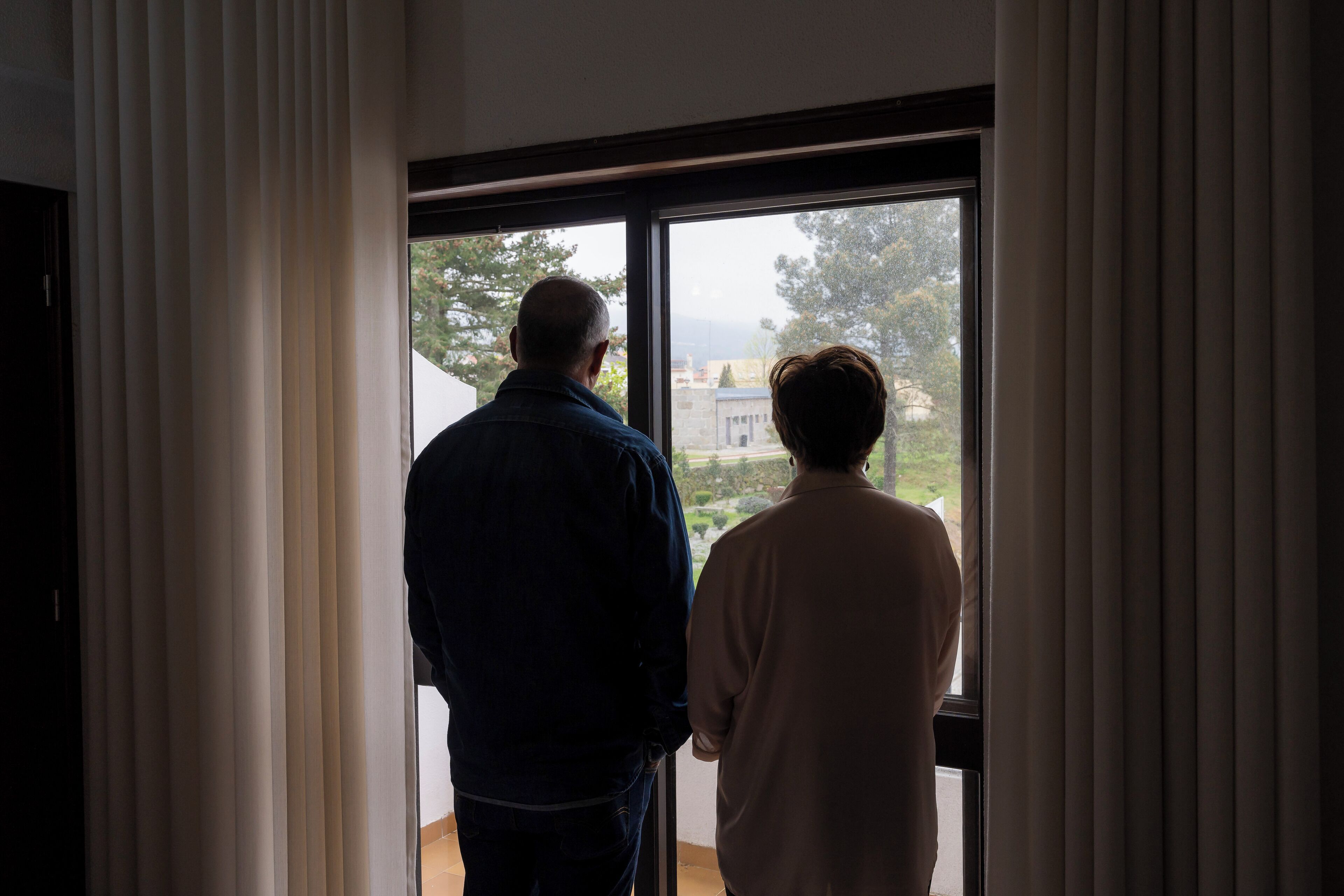 Dos personas de pie junto a una ventana, mirando hacia el exterior.