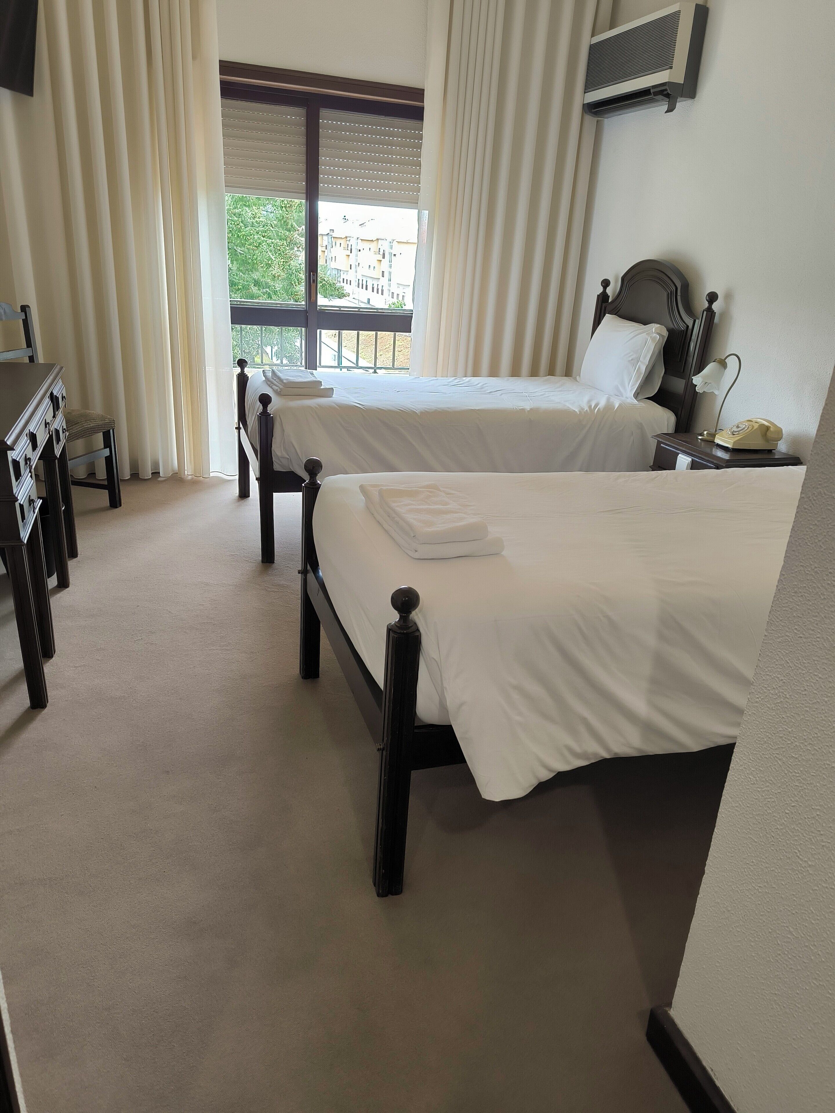 Habitación de hotel con dos camas, un escritorio, una silla y una ventana con cortinas.