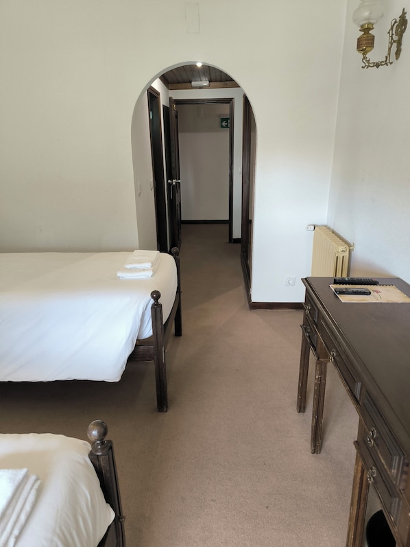 Une chambre d’hôtel avec un lit, un bureau et une porte en arc donnant sur un couloir.