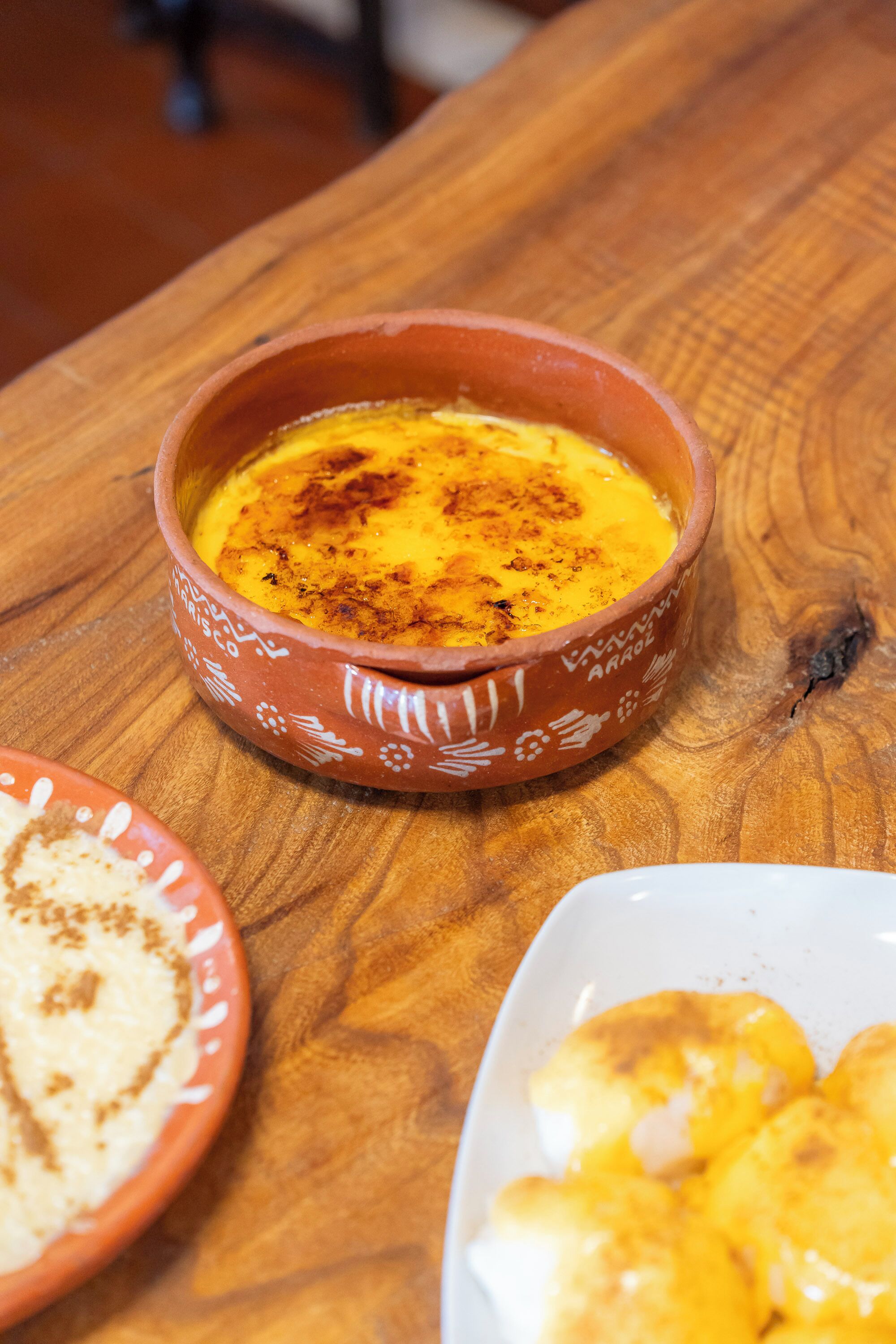 Un tazón de terracota con un plato cremoso, posiblemente un postre, sobre una mesa de madera.