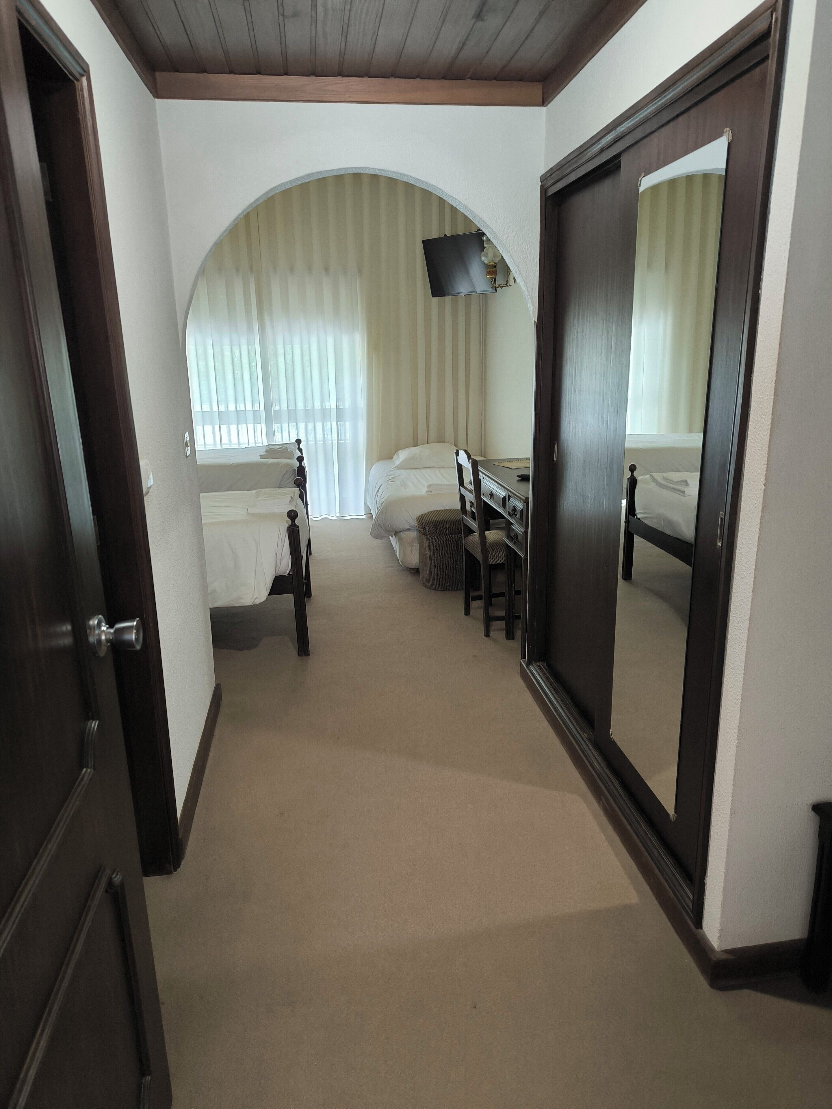 A hotel room with a bed, a desk, a chair, a TV, and a large mirror.