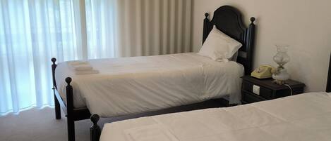 Two single beds with wooden headboards, a bedside table with a lamp, and a wall-mounted air conditioner.