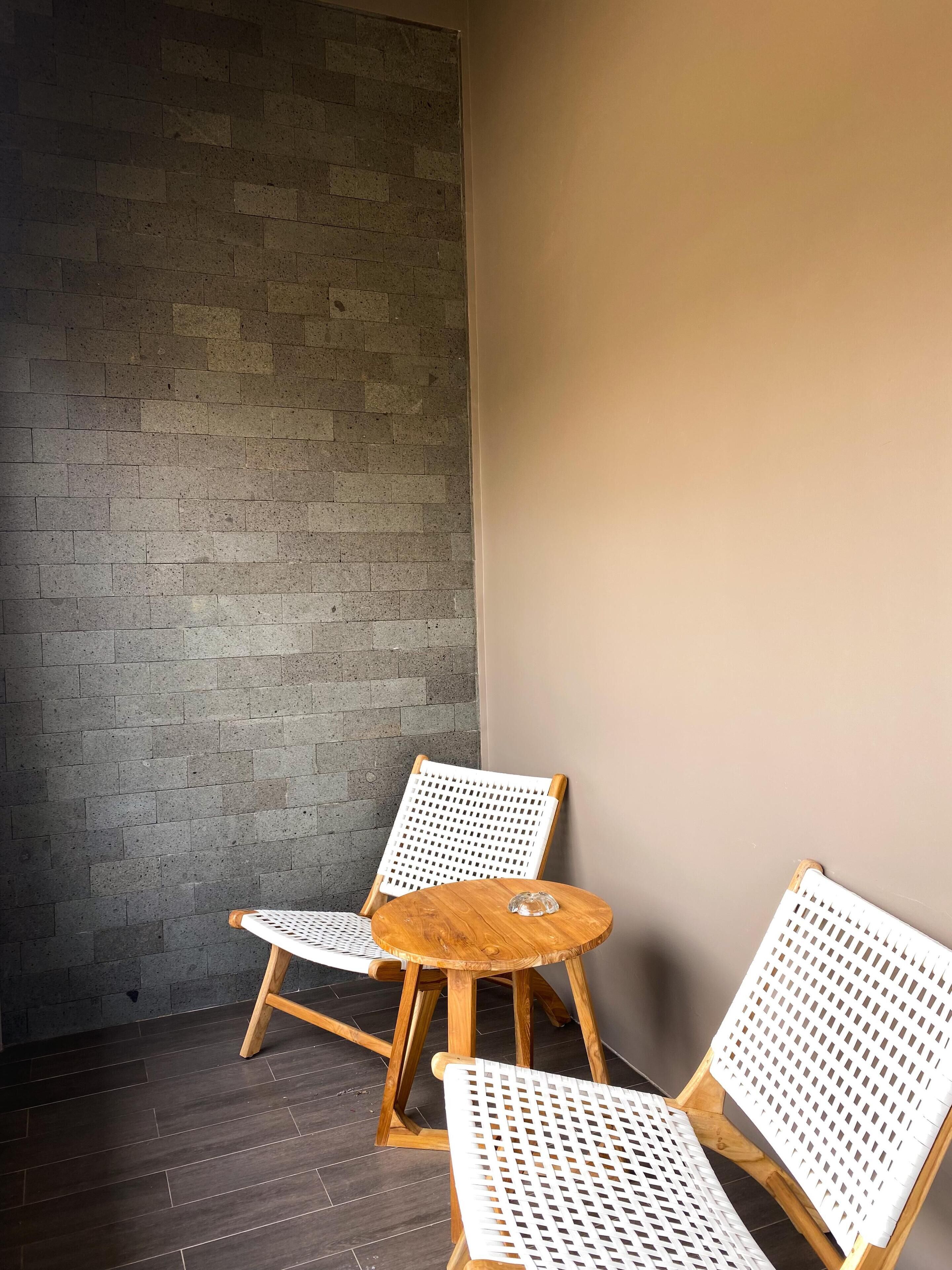 Rincón con dos sillones blancos de mimbre y una pequeña mesa redonda de madera.