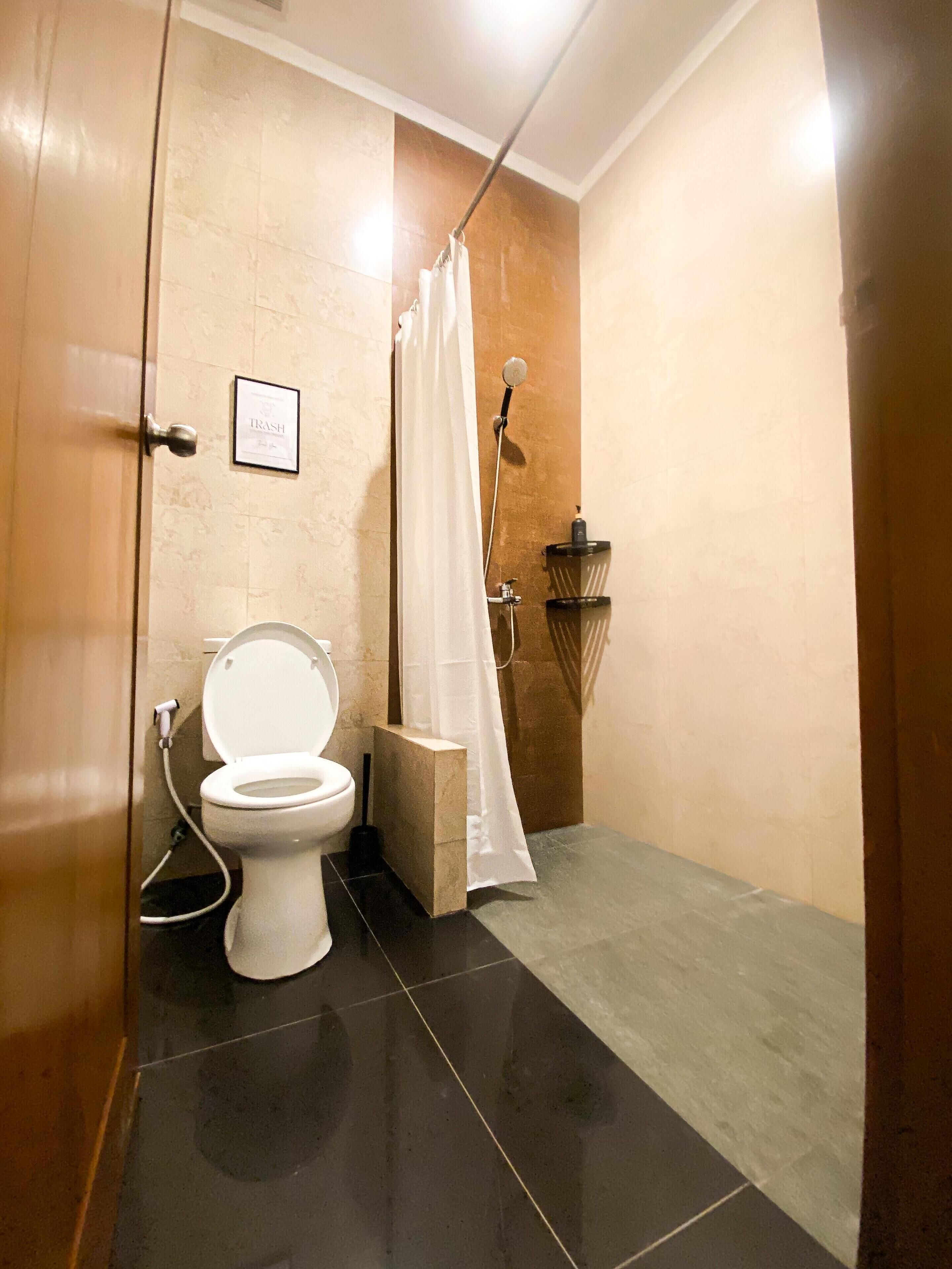 A bathroom with a toilet, a shower, and a trash bin.