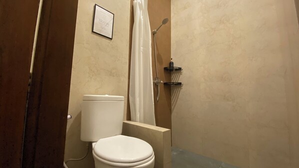 A bathroom with a toilet, a shower with a curtain, and a wall-mounted shelf.