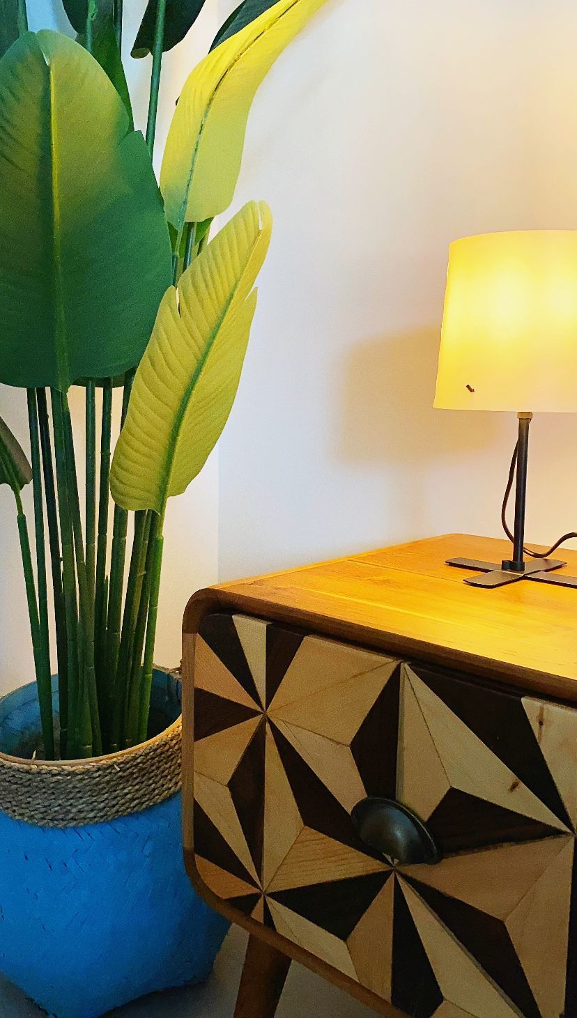 Una stanza con un tavolino in legno, una lampada e un vaso blu con foglie verdi.