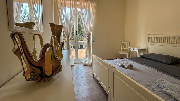 A bedroom with a bed, a chair, a desk, and a mirror. There is a balcony with curtains and a view of the outside. - [BGY/CITY] Comfortable apartment in the BORGO (Bergamo)