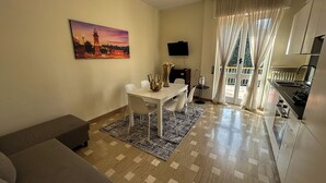 A modern living room with a sofa, a dining table with chairs, a TV mounted on the wall, and a kitchen area with a stove. - [BGY/CITY] Comfortable apartment in the BORGO (Bergamo)