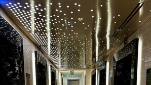 Un corridoio moderno e luminoso con pavimenti e pareti in marmo, dotato di diversi ascensori e una porta in fondo.