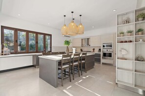 A modern kitchen with a central island, built-in appliances, and a dining area with a view of the outdoors. - The Tides | Beach Club, Housekeeping & Beach Walk! (Las Golondrinas 21, Hacienda Pinilla)