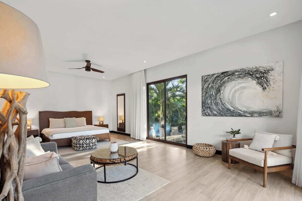 A modern hotel room with a large bed, a seating area with a round coffee table, and a large abstract painting on the wall.