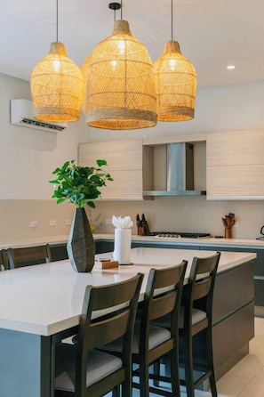 A modern kitchen with a central island, dark wooden chairs, and three woven pendant lights. - The Tides | Beach Club, Housekeeping & Beach Walk! (Las Golondrinas 21, Hacienda Pinilla)