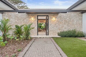 A modern building entrance with a stone facade, a paved pathway leading to the door, and a well-maintained lawn. - The Tides | Beach Club, Housekeeping & Beach Walk! (Las Golondrinas 21, Hacienda Pinilla)