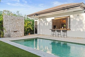 A modern house with a swimming pool, stone wall, and outdoor bar area.