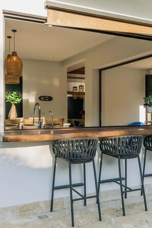 A modern kitchen with a bar area, two bar stools, and hanging pendant lights. - The Tides | Beach Club, Housekeeping & Beach Walk! (Las Golondrinas 21, Hacienda Pinilla)