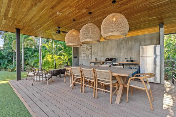 An outdoor patio with a wooden deck, wicker chairs, a dining table, and a built-in grill.