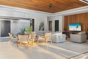 A modern living room with a stone wall, wooden ceiling, and a large flat-screen TV. - The Tides | Beach Club, Housekeeping & Beach Walk! (Las Golondrinas 21, Hacienda Pinilla)