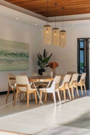 A modern dining area with a wooden table and chairs, pendant lights, and a large abstract painting on the wall.