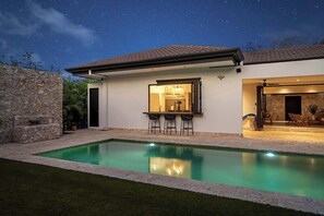 A modern house with a swimming pool, stone walls, and a patio area with outdoor seating. - The Tides | Beach Club, Housekeeping & Beach Walk! (Las Golondrinas 21, Hacienda Pinilla)