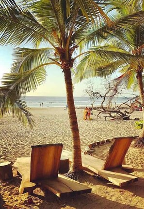 A beach with wooden lounge chairs, palm trees, and a clear view of the ocean. - The Tides | Beach Club, Housekeeping & Beach Walk! (Las Golondrinas 21, Hacienda Pinilla)