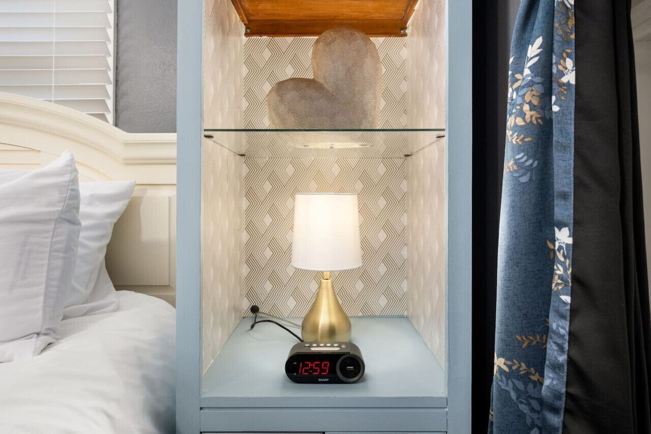 Une table de chevet avec une horloge numérique, une lampe et une étagère en verre.