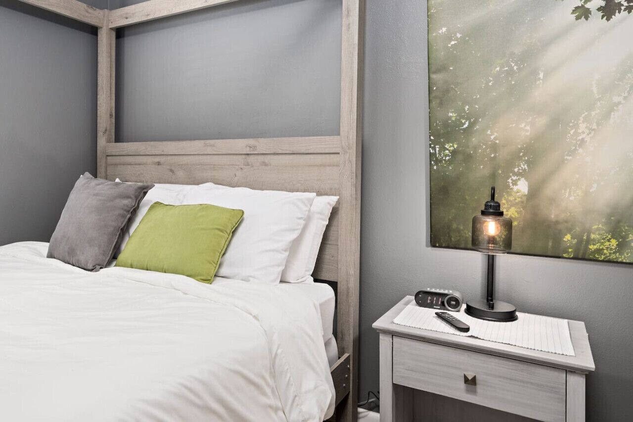 A bedroom with a bed, pillows, a nightstand, a lamp, and a wall-mounted picture.